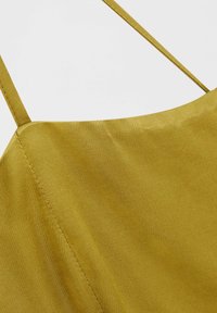 Haut sans manches jaune moutarde avec une texture satinée lisse et un décolleté droit, doté de fines bretelles et de détails de couture subtils.