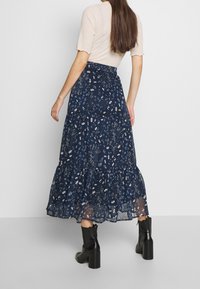 Laivastonsininen kukkakuosis maxi-hame, jossa on kerroksellisia taitoksia ja kevyttä kangasta. Varustettuna röyhelöreunalla ja joustavalla vyötäröllä. Yhdistettynä mustiin nilkkabootseihin.