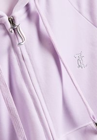 Felpa con zip di colore lilla, dotata di una zip in metallo argento, cuciture tono su tono e un logo testurizzato sul petto. Tessuto morbido e liscio.