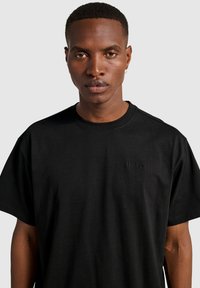 Czarna bawełniana koszulka z okrągłym dekoltem i krótkimi rękawami, z subtelnym logo HALO w tonowej haftowanej aplikacji na piersi.