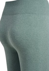 Nærbillede af ribbed grønne leggings med høj talje og tætsiddende stof, der former hofter og lår.