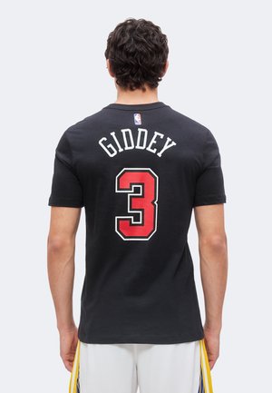 Homme portant un maillot de basket noir avec "Giddey" et le numéro 3 en rouge dans le dos, debout de dos sur un fond uni.