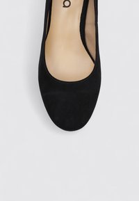 Ballerine en suède noir avec un bout arrondi et un design minimaliste. Texture lisse avec une semelle intérieure légèrement rembourrée visible.
