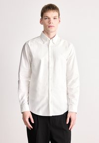 Λευκό πουκάμισο με μακριά μανίκια και κουμπιά, κατασκευασμένο από βαμβάκι. Διαθέτει μυτερό γιακά και μικρό λογότυπο στο στήθος. Λεία υφή και κλασική εφαρμογή.