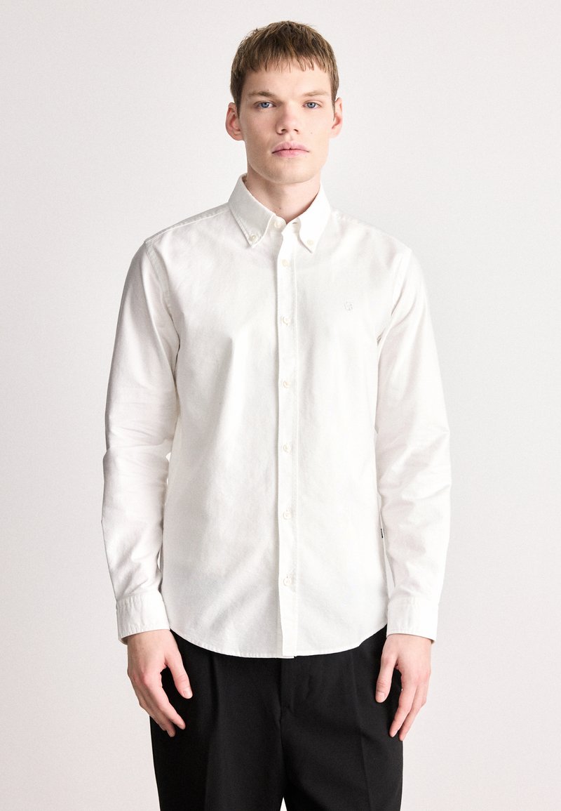 Λευκό πουκάμισο με μακριά μανίκια και κουμπιά, κατασκευασμένο από βαμβάκι. Διαθέτει μυτερό γιακά και μικρό λογότυπο στο στήθος. Λεία υφή και κλασική εφαρμογή.