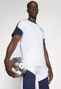 Korte mouwen witte voetbalshirt met marineblauwe accenten, gecombineerd met witte shorts met marineblauwe geometrische panelen, vastgehouden met een patroonvoetbal.