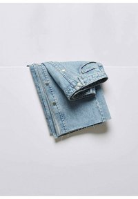 Veste en jean bleu clair pliée avec des boutons-pression argentés visibles, posée sur une surface blanche.