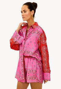 Conjunto de top y pantalones cortos coloridos con patrones de paisley en rosa y rojo, con un cuello tipo camisa y cinturilla elástica. Textura sedosa.