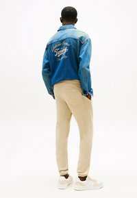 Denim jacket met geborduurd 'Tommy' logo in beige. Beige sweatpants met zijzakken. Witte sneakers met beige accenten.