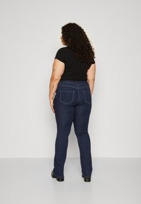 Jeans de mezclilla azul oscuro con forma ajustada, cintura media y dos bolsillos traseros. La tela tiene una textura suave y un ligero estiramiento.