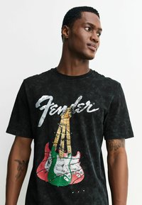 Czarny t-shirt z wyblakłą fakturą, z grafiką czterech gitar elektrycznych w kolorach zielonym, białym i czerwonym, z logo "Fender" powyżej.