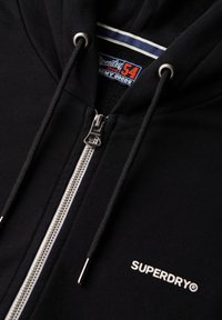 Felpa nera con zip in cotone. Presenta una cerniera argento, una fodera interna bianca e un logo ricamato. Include lacci con punte metalliche.