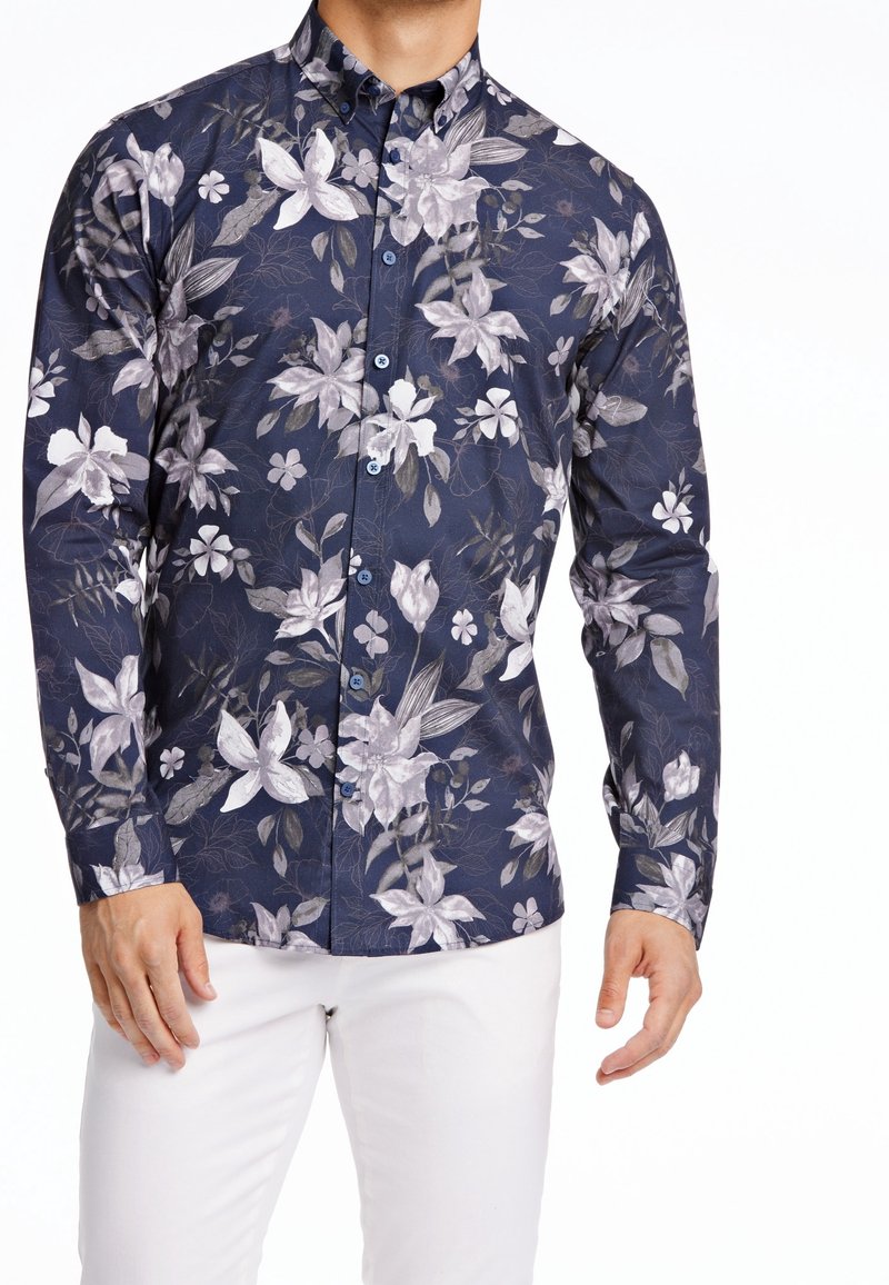 Camisa de manga larga confeccionada con tela que presenta un fondo azul marino oscuro con grandes motivos florales en gris y blanco, cuello abotonado y botones azules.