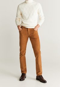 Beige Cordhosen mit schlanker Passform, kombiniert mit einem cremefarbenen Rollkragenpullover mit einem strukturierten Rautenmuster. Braune Stiefeletten inklusive.