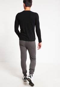 Top negro de manga larga y pantalones jogger grises con puños, combinados con zapatillas blancas. Textura suave y diseño ajustado. Estilo sencillo y casual.