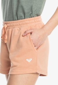Perzikkleurige katoenen shorts met een elastische tailleband, een trekkoord en zijzakken. Witte hartlogo detail aan de onderzoom.