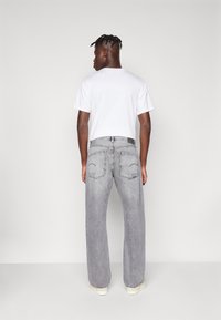 Jeans anchos grises con un acabado deslavado, que presentan bolsillos traseros con detalles de costura sutil, combinados con una camiseta blanca lisa.