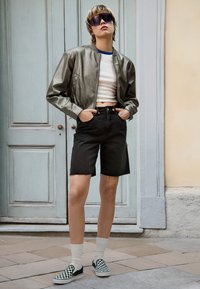 Metallinen hopeinen bomber-takki, valkoinen lyhyt toppi, mustat farkkushortsit ja ruudulliset slip-on-kengät. Vaaleanharmaat sukat viimeistelevät asun.