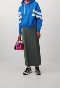 Blauwe hoodie met witte strepen, groene maxi-rok, roze handtas en zwarte sneakers. Glad textuur en casual ontwerp.