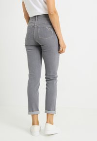 Vaqueros de mezclilla gris con cintura alta, corte ajustado, puños doblados y dos bolsillos traseros. La tela tiene una textura suave y un ligero estiramiento.