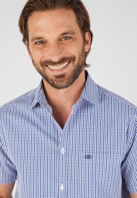 Camicetta a maniche corte a quadretti blu e bianchi, con colletto abbottonato, taschino frontale e logo ricamato sul petto.