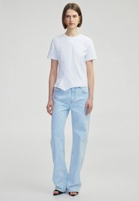 Camiseta blanca de manga corta con bajo recto, combinada con jeans de color azul claro que presentan un patrón en forma de chevron y piernas ligeramente acampanadas. Sandalias negras de punta abierta.