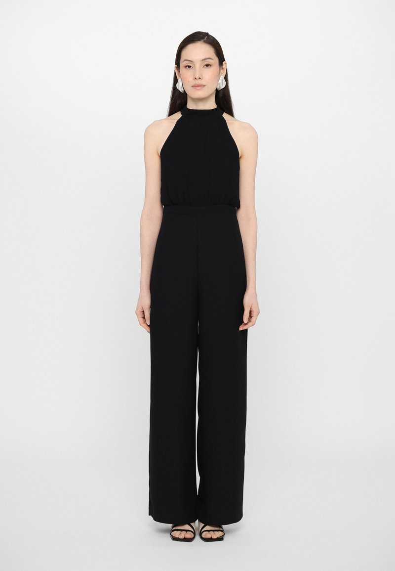 Svart halter jumpsuit med vide ben, glatt tekstur, rynket bodice og en smal midje. Enkel design kombinert med svarte sandaler.