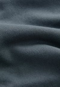 Donkergrijze stof met een geribbelde textuur, die plooien en een lichte glans toont, wat wijst op een zachte, rekbare materiaal dat geschikt is voor kleding.