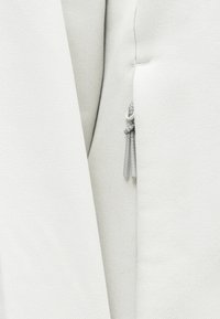 Gros plan d’un tissu gris clair avec un petit cordon bouclé noué sur un fond texturé uni.