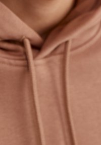Sudadera de color rosa claro con un cuello ajustable, textura de tela suave y costuras bien definidas. El enfoque está en la parte superior cerca del escote.