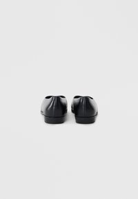Ballerines en cuir noir avec une texture lisse, bout rond, talon bas et design minimaliste. Pas de quincaillerie ou d'accents visibles.