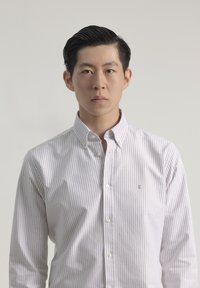 Camisa de botones a rayas ligeras hecha de algodón en blanco y beige claro. Presenta un cuello abotonado y un pequeño logo bordado en el pecho.