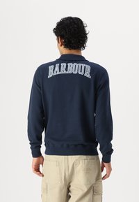 Tengerészkék pulóver, bordás mandzsettákkal és aljjal, a hátsó részén világoskék betűkkel a 'BARBOUR' felirattal. Pamut keverék anyag.