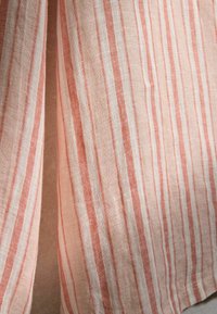 Tissu léger à rayures verticales dans des tons de rose, beige et blanc, suspendu librement avec un espace visible entre.