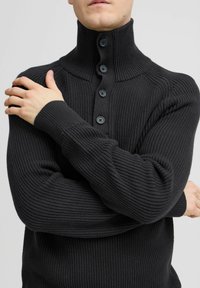 Pulover negru tricotat cu un guler înalt, cinci nasturi frontal, și mâneci ajustate, evidențiind un material texturat și un design structurat.