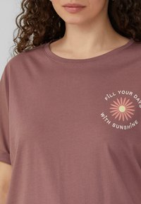 Licht mauve t-shirt van zacht stof. Heeft een ronde halslijn en korte mouwen, met een bloemenpatroon en tekst op de borst.