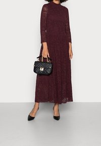 Burgundy spets maxiklänning med långa ärmar, prydd med blommönster. Utrustad med en svart kviltad handväska och svarta spetsiga klackar.