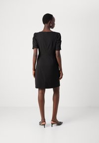 Vestito nero a maniche corte con silhouette aderente, scollatura quadrata e chiusura con cerniera sul retro. Presenta dettagli arricciati sulle maniche e lunghezza fino a metà coscia.