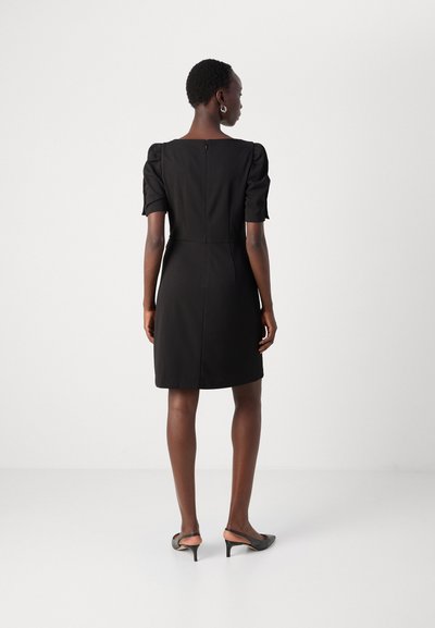 Robe noire à manches courtes avec une silhouette ajustée, décolleté carré et fermeture éclair dans le dos. Présente des détails froncés sur les manches et une longueur mi-cuisse.