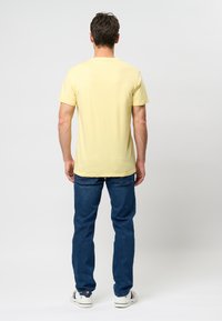 Tricou scurt cu mânecă galben, din bumbac, croială slim, asortat cu blugi albaștri, stil casual, design simplu, fără logo-uri sau modele vizibile.