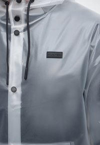 Γκρι διάφανο αδιάβροχο με μαύρα κουμπιά, μαύρα κορδόνια και μαύρο ορθογώνιο λογότυπο «Hunter» στο στήθος.