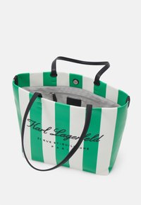 Grand sac fourre-tout rayé vert et blanc avec anses noires, ouverture en haut et poche intérieure zippée, avec le logo Karl Lagerfeld sur le devant.