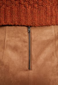 Jupe en suède marron avec une fermeture éclair, accompagnée d'un pull en tricot orange en haut, affichant un motif texturé et côtelé.