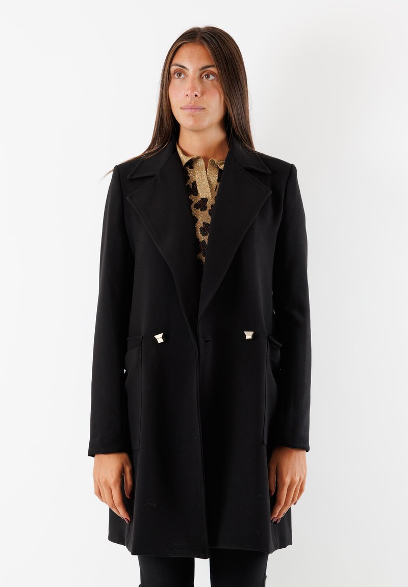 Cappotto in lana nera con design sartoriale, maniche lunghe e dettagli in metallo dorato sui taschini. Presenta un colletto a scollo a V e linee pulite.