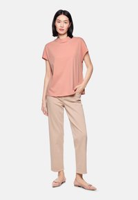 Pink short-sleeve top with a high neckline and subtle embellishments, paired with light beige straight-leg trousers and pink flats.