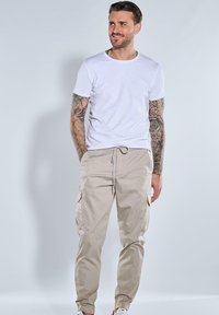 Weißes Kurzarm-T-Shirt kombiniert mit beigen Cargo-Hosen mit Seitentaschen. Das Outfit umfasst weiße Sneaker und hat eine lässige Passform.