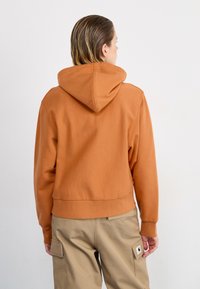 Cotton hoodie in warm brown with a hood, ribbed cuffs, and cropped hem. Paired with beige cargo pants featuring side pockets.