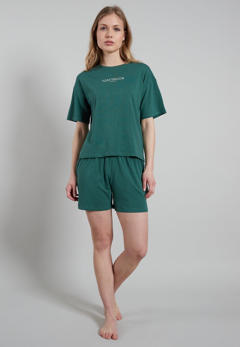 Green cotton loungewear set featuring a loose short-sleeve T-shirt with logo and matching shorts. Both are simple and soft-textured.