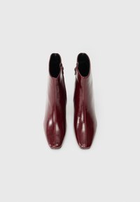 Μπορντό δερμάτινα μποτάκια αστραγάλου με λεπτό, μυτερό σχέδιο στη μύτη και πλαϊνά φερμουάρ για εύκολη φορεσιά. Λείο υλικό, μινιμαλιστικό στυλ.