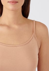 Canotta nuda con spalline sottili. Realizzata in un tessuto morbido e elastico con una texture liscia e un girocollo arrotondato, caratterizzata da dettagli di cucitura discreti.